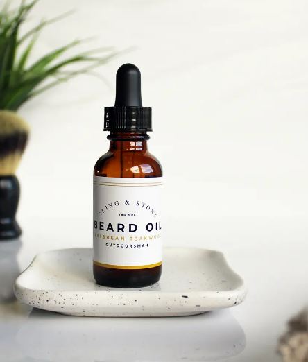 A bottle of beard oil placed on a ceramic tray with grooming accessories in the background, suggesting a men's grooming routine.